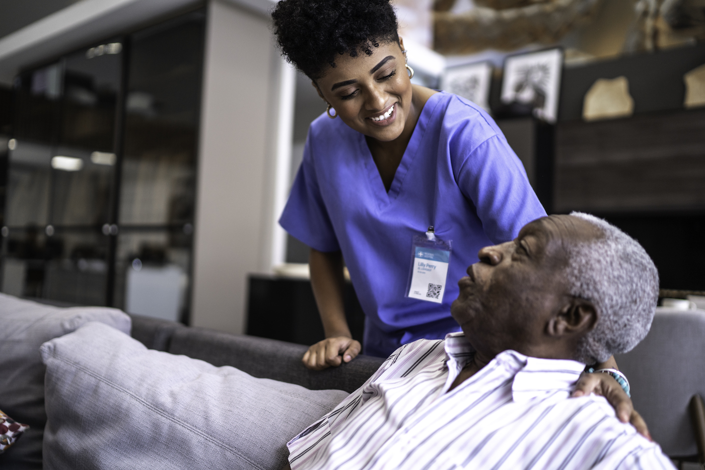 Female nurse taking care of a senior man at home Female nurse in blue scrubs taking care of a senior man at home sitting on couch