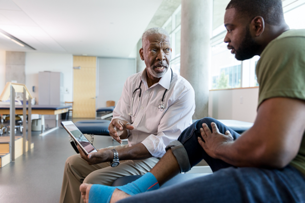 Picture2 African-American doctor reading information from tablet to African-American patient sitting on bench in doctor's office